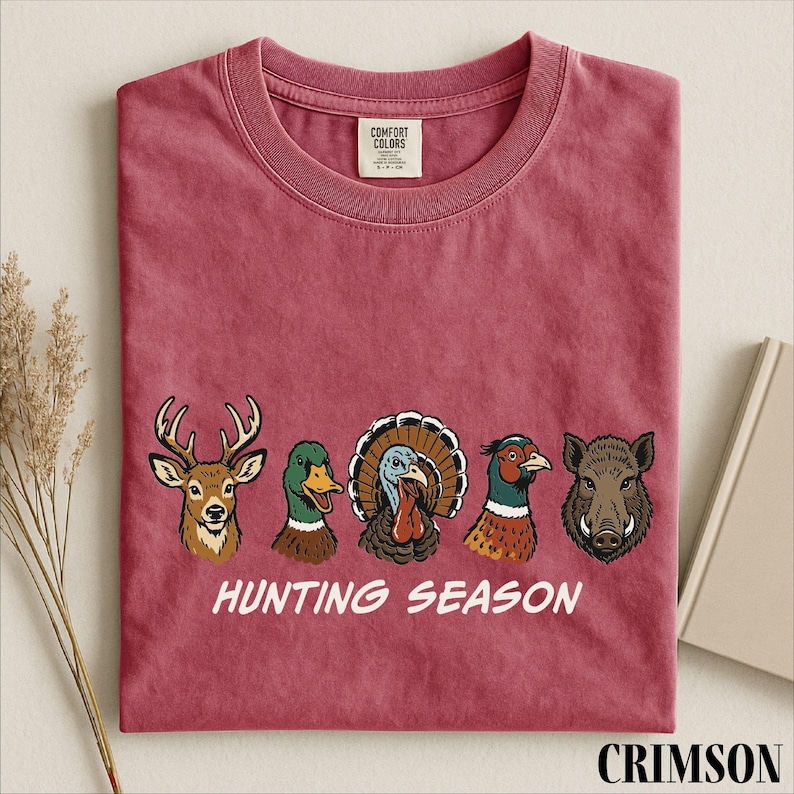 A red t-shirt with a graphic design of five animal heads, including a deer, duck, turkey, boar, and pheasant, along with the text "HUNTING SEASON".
