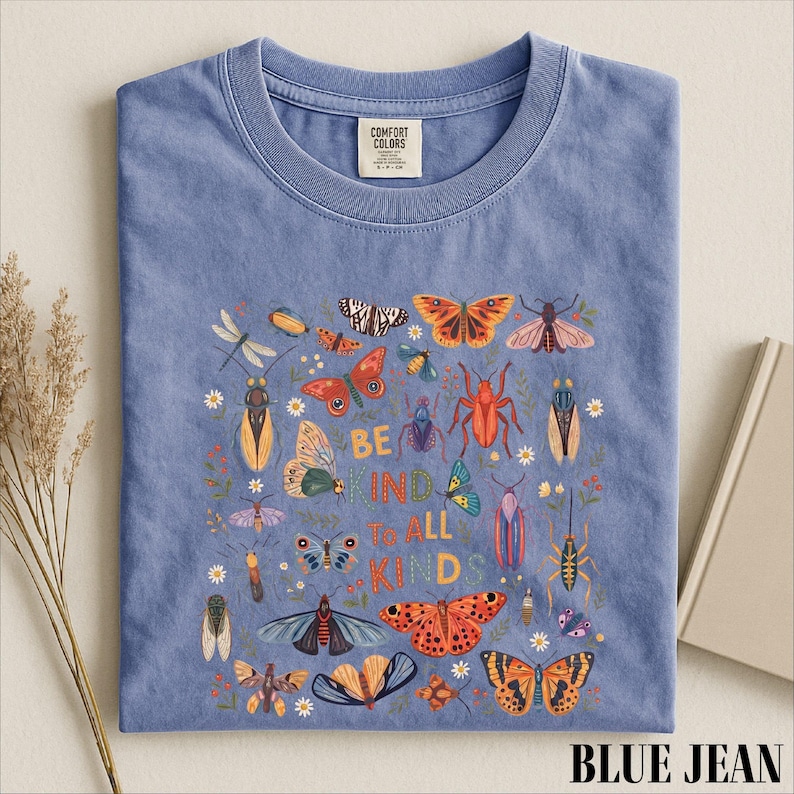 A blue t-shirt with a colorful graphic design featuring various insects and butterflies, along with the text "Be kind to all kids".