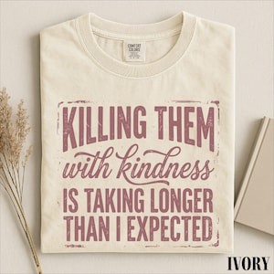 A white t-shirt with a printed message that reads "Killing them with kindness is taking longer than I expected".