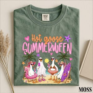May include: A sage green t-shirt featuring the text "Hot goose SUMMERWEEN" in orange and pink. The graphic depicts four white geese on a beach, with one wearing a ghost costume, one in a bikini, and two wearing sunglasses and sun hats.