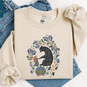 a beige t-shirt with a colorful floral design and a black bear illustration, along with a pair of blue jeans.