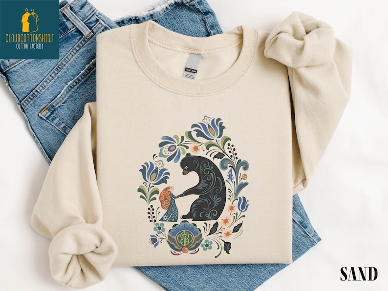 a beige t-shirt with a colorful floral design and a black bear illustration, along with a pair of blue jeans.