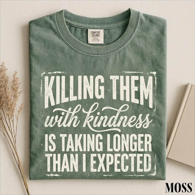 A green t-shirt with a white text design that reads "Killing them with kindness is taking longer than I expected".