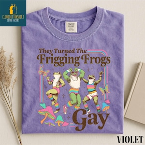 Pu&ograve; includere: T-shirt viola con una grafica di tre rane danzanti in abiti colorati, il testo recita "They Turned The Frigging Frogs Gay". La maglietta ha un'etichetta Comfort Colors.