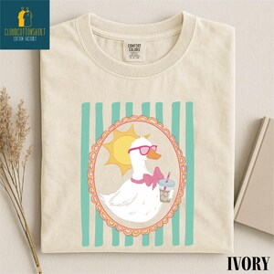 a white t-shirt with a colorful graphic design depicting a duck wearing sunglasses and holding a drink.