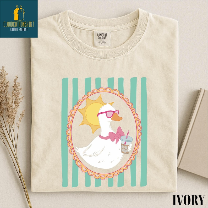 a white t-shirt with a colorful graphic design depicting a duck wearing sunglasses and holding a drink.