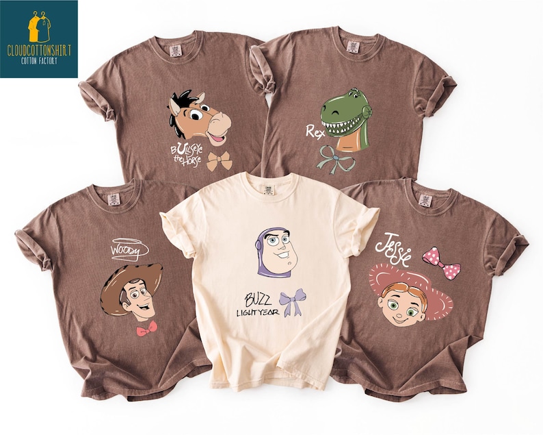 A collection of five t-shirts with cartoon character designs, including a cowboy, a dinosaur, and a girl.