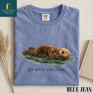 A blue t-shirt with an illustration of an otter and the text "go with the flow" printed on it.
