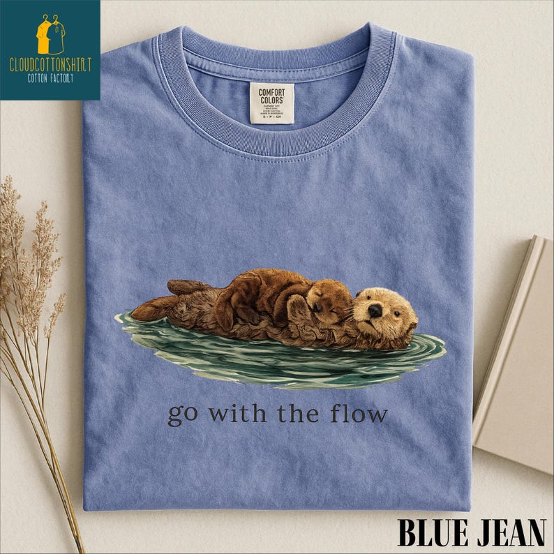 A blue t-shirt with an illustration of an otter and the text "go with the flow" printed on it.