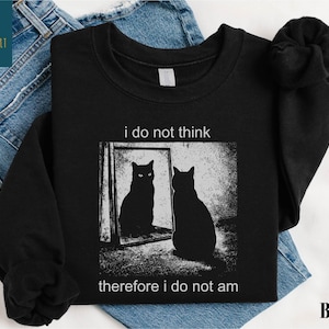 May include: Black sweatshirt with a graphic of a cat looking in a mirror, with the text "i do not think therefore i do not am". The sweatshirt is displayed on a pair of blue jeans.