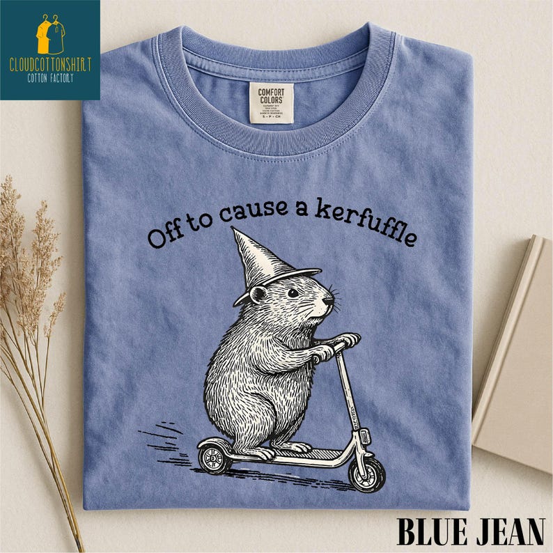A blue t-shirt with a cartoon image of a hamster riding a scooter, along with the text "Off to cause a kerfluffle" printed on it.