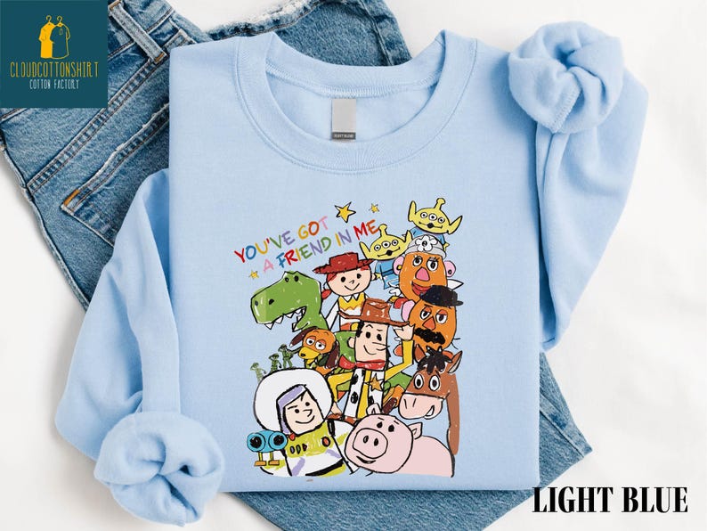 K&ouml;nnte beinhalten: Hellblaues Sweatshirt mit einer bunten Grafik von Figuren aus dem Film "Toy Story". &Uuml;ber den Figuren steht der Schriftzug "YOU'VE GOT A FRIEND IN ME". Das Sweatshirt ist aus weichem Material.