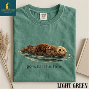 A green t-shirt with an illustration of an otter and the text "go with the flow" printed on it.