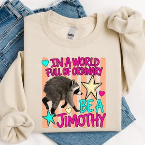 A beige t-shirt with a colorful graphic design and text printed on it, along with a pair of blue jeans.