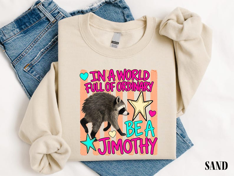 A beige t-shirt with a colorful graphic design and text printed on it, along with a pair of blue jeans.