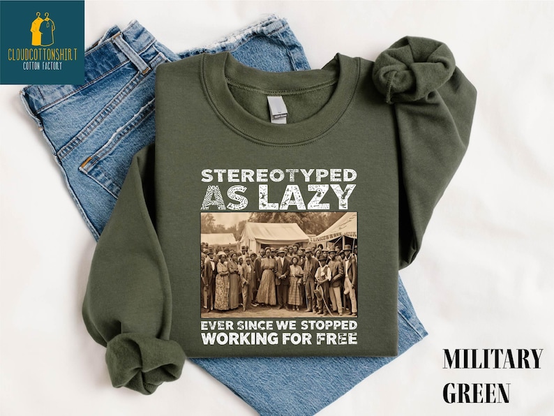 May include: Military green sweatshirt with the text "STEREOTYPED AS LAZY" above a sepia-toned image of a group of people. Below the image is the text "EVER SINCE WE STOPPED WORKING FOR FREE". The sweatshirt is displayed on top of blue jeans.