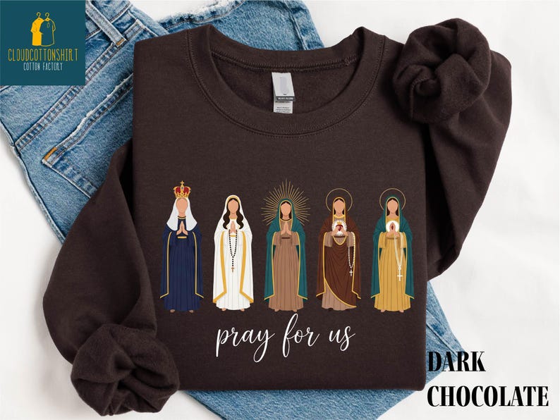 May include: Dark chocolate-colored sweatshirt featuring an illustration of five religious figures. The figures are depicted in various robes and headdresses, with the words "pray for us" in cursive script below. The words "DARK CHOCOLATE" are printed in a block font.