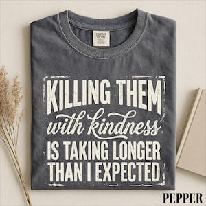 A gray t-shirt with a white text design that reads "Killing them with kindness is taking longer than I expected".