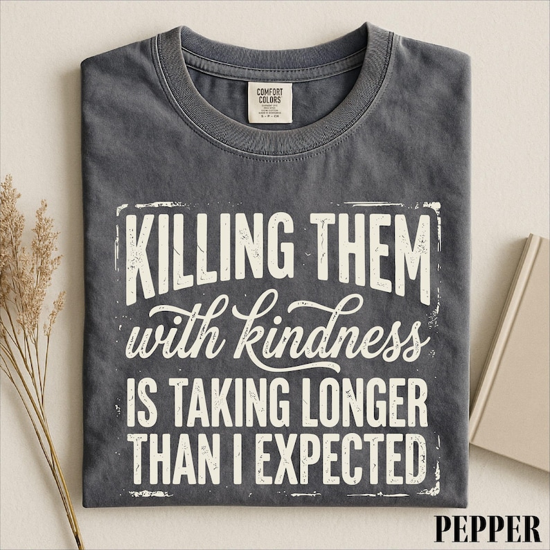 A gray t-shirt with a white text design that reads "Killing them with kindness is taking longer than I expected".