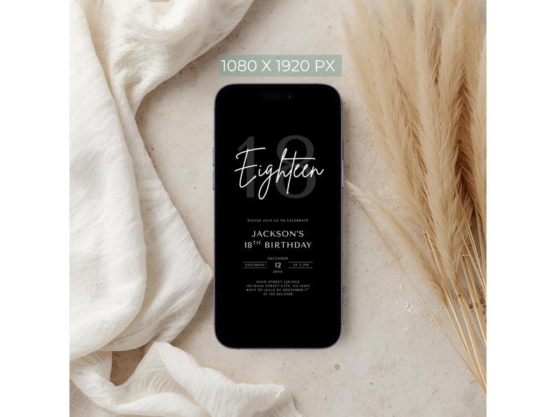 May include: A black smartphone displays a birthday invitation. The invitation reads "Eighteen" in cursive above "Jackson's 18th Birthday" with date and time details. The phone is set against a neutral background with fabric and dried plants.