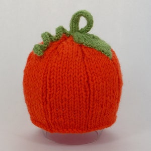 May include: Orange knitted pumpkin hat with a green knitted stem and leaf detail.