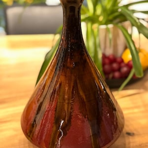 Peut inclure: Un vase en céramique émaillée fait à la main, de forme unique. Le vase présente un col marron foncé qui se transforme en un corps brun rougeâtre avec des stries verticales orange et jaune. Le vase a une finition brillante et convient à la décoration intérieure.