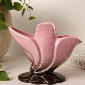 Peut inclure: Un vase en céramique rose avec un design floral unique et stylisé. Le vase a une finition mouchetée et une base marron foncé. Le design présente des formes incurvées en forme de pétales, créant une apparence élégante et artistique. C'est un objet de décoration.