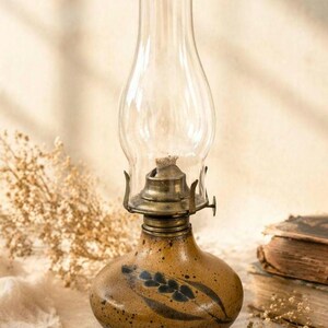 May include: A vintage oil lamp with a clear glass chimney and a speckled brown ceramic base. The base features a hand-painted design of blue leaves. The lamp has a brass fitting and is designed for oil.