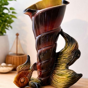 May include: A ceramic vase with a fish and shell design. The vase is brown, red, and yellow. The vase has a fish at the base and a shell-like form. The vase is a decorative item, suitable for display. The vase is approximately 25 cm tall.