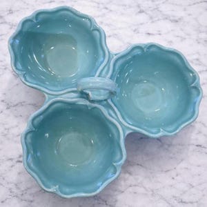 Peut inclure: Plat de service en céramique turquoise à trois compartiments. Chaque compartiment est un bol festonné, relié par une poignée centrale. La finition est brillante, parfait pour servir des collations ou des apéritifs.