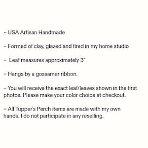Op de afbeelding: Een handgemaakt klei-ornament in de vorm van een blad, ongeveer 7,6 cm lang. Het object heeft een geglazuurde afwerking en hangt aan een ragfijn lint. De tekst op de afbeelding luidt: USA Artisan Handmade, Formed of clay, glazed and fired in my home studio, Leaf measures approximately 3, Hangs by a gossamer ribbon, You will receive the exact leaf/leaves shown in the first photos. Please make your color choice at checkout, All Tupper's Perch items are made with my own hands. I do not participate in any reselling.