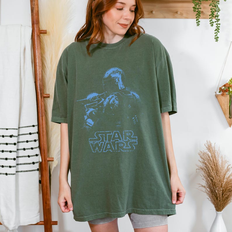 Puede incluir: Una camiseta de manga corta color verde oliva con un estampado gr&aacute;fico azul de The Mandalorian y Grogu. El dise&ntilde;o incluye el logotipo de Star Wars en una fuente azul desgastada centrada en el pecho. La camiseta tiene cuello redondo.