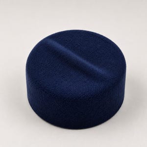 Könnte beinhalten: Ein marineblauer, zylindrischer Hut mit strukturierter Oberfläche und einer vertieften Linie über der Oberseite. Der Hut ist einfarbig und liegt auf einem weißen Hintergrund. Der Hut scheint aus einem weichen Material zu sein.