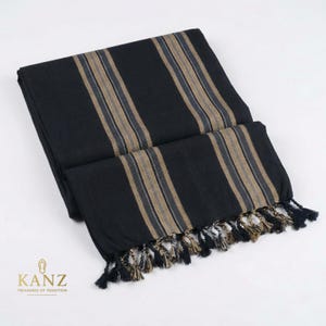Könnte beinhalten: Ein gefaltetes schwarzes Textil mit vertikalen Streifen in Beige und Grau. Das Textil hat unten eine Fransenquaste. Das Logo "KANZ TREASURES OF TRADITION" befindet sich in der unteren linken Ecke.