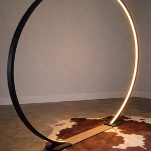 May include: A modern black floor lamp with a curved, illuminated design. The lamp has a warm, yellow glow and stands on a wooden base. The lamp is set on a cowhide rug.