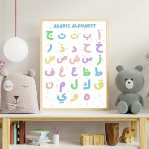 Peut inclure: Une affiche encadrée avec l'"ARABIC ALPHABET" présente des lettres arabes colorées sur fond blanc avec des éclaboussures pastel. Les lettres sont de différentes couleurs, dont le bleu, le vert et le rose. L'affiche est sur une étagère en bois avec des jouets.