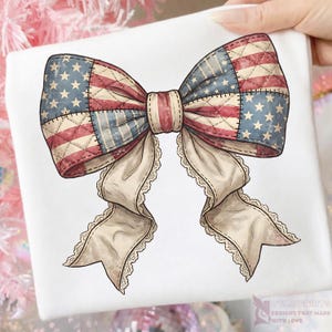 Può includere: Un design di fiocco patriottico con la bandiera americana. Il fiocco ha un design patchwork con colori rosso, bianco e blu. I nastri del fiocco sono color crema con un bordo in pizzo. Il design è su sfondo bianco.