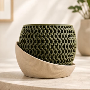 May include: A round olive green planter featuring a complex, repeating wave-like lattice pattern. The planter is cradled within a textured, beige, asymmetrical base that curves upward along one side, providing a stable foundation for the pot.