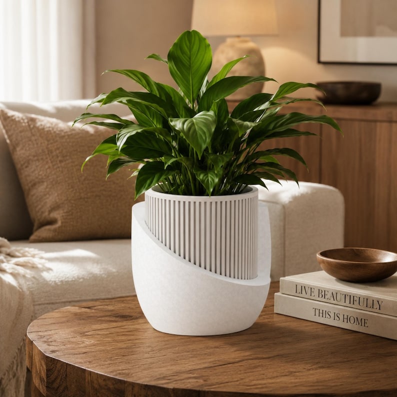 May include: A vibrant green peace lily plant potted in a white planter with a textured, vertical slatted inner cylinder and a smooth, curved outer shell. The plant features broad, pointed leaves that extend upward from the center of the container.