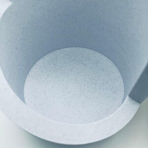 May include: A light blue cylindrical container with a speckled texture throughout its surface. The interior base features visible concentric circular ridges, and the walls show a layered construction pattern consistent with 3D printing.