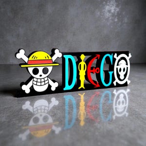 May include: A black wooden sign featuring the word "DIEGO" in colorful letters, with a skull and crossbones logo on the left and right. The "D" is blue, the "I" is yellow, the "E" is red, the "G" is blue, and the "O" is white.
