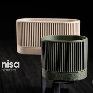 May include: Two modern planters with vertical ribbed detailing. One is a light beige oval shape, and the other is a dark olive green cylindrical shape. The planters are set against a dark background, showcasing their contemporary design. The brand name "nisa planters" is visible.