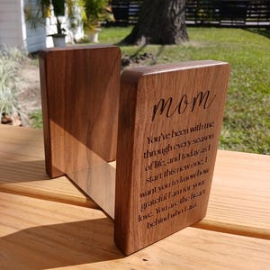 May include: A wooden bookend set with a warm brown finish. The bookends are angled and feature the word "mom" and a heartfelt message engraved on one side. The bookends are designed to hold books and add a decorative touch.