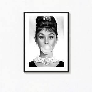 May include: Black and white framed print of a woman blowing a bubble. The woman has dark hair styled in an updo, pearl earrings, and a pearl necklace. The image is a portrait with a black frame.