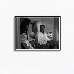 May include: Black and white framed print of a scene from a movie. A man in a white shirt sits on a toilet, while another man in a jacket stands in the doorway. A towel rack and a cabinet are visible in the background.