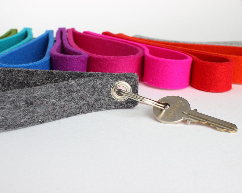 Puede incluir: Un llavero de fieltro gris con un anillo de metal y una llave plateada. El llavero est&aacute; rodeado por una franja de fieltro arco&iacute;ris de varios colores, incluyendo verde, azul, morado, rosa, rojo, naranja y gris.
