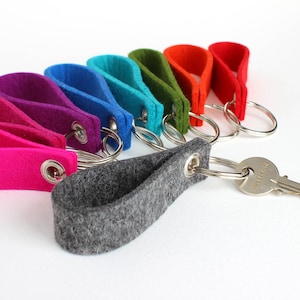 May include: A set of colorful felt keychains with a gray felt keychain with a metal ring and key attached. The keychains are in a rainbow order, starting with pink and ending with green.