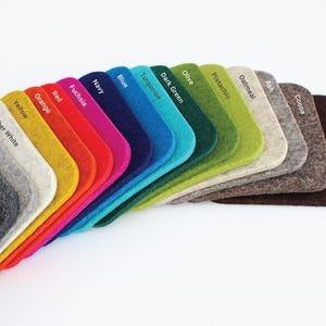 May include: A fan-shaped arrangement of rectangular felt swatches with rounded corners, each labeled with color names including Basalt, Charcoal, Gray, Heather White, Yellow, Orange, Red, Fuchsia, Navy, Blue, Turquoise, Dark Green, Olive, Pistachio, Oatmeal, Ash, Cocoa, and Dark Brown.