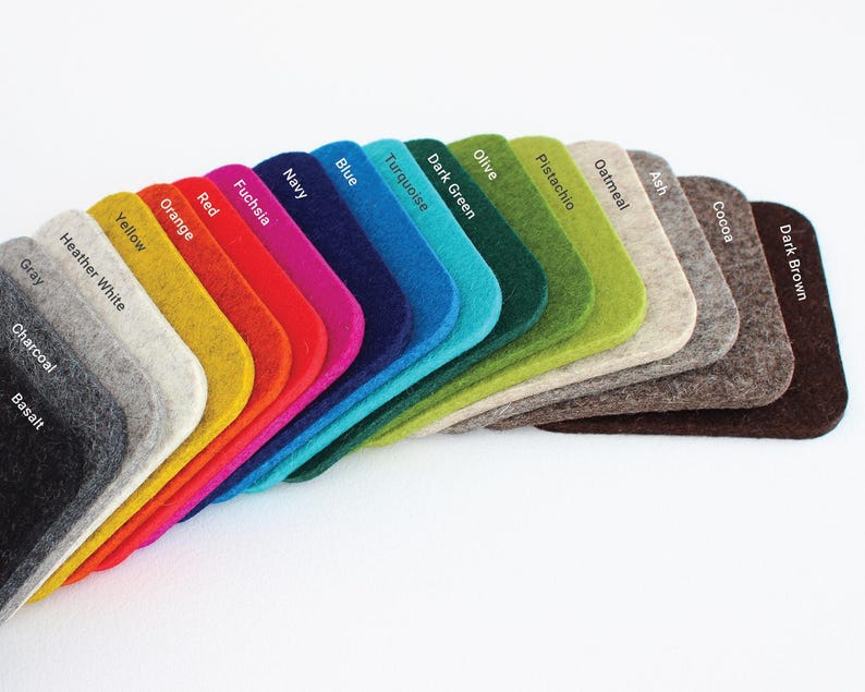 May include: A fan-shaped arrangement of rectangular felt swatches with rounded corners, each labeled with color names including Basalt, Charcoal, Gray, Heather White, Yellow, Orange, Red, Fuchsia, Navy, Blue, Turquoise, Dark Green, Olive, Pistachio, Oatmeal, Ash, Cocoa, and Dark Brown.