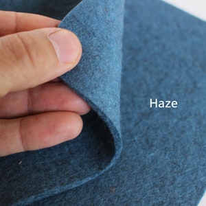 K&ouml;nnte beinhalten: Nahaufnahme eines dunkelblauen Filzstoffs mit dem aufgedruckten Wort "Haze". Der Stoff wird von einer Hand gehalten, wodurch seine Textur sichtbar wird.